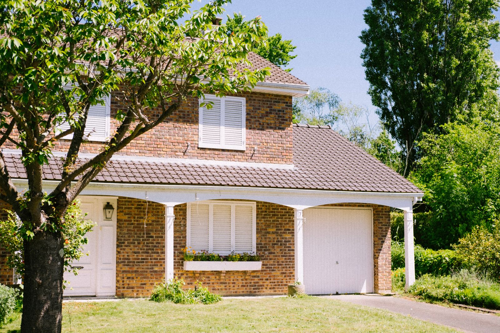 A sunny view of a classic two-story brick house with a lush garden.