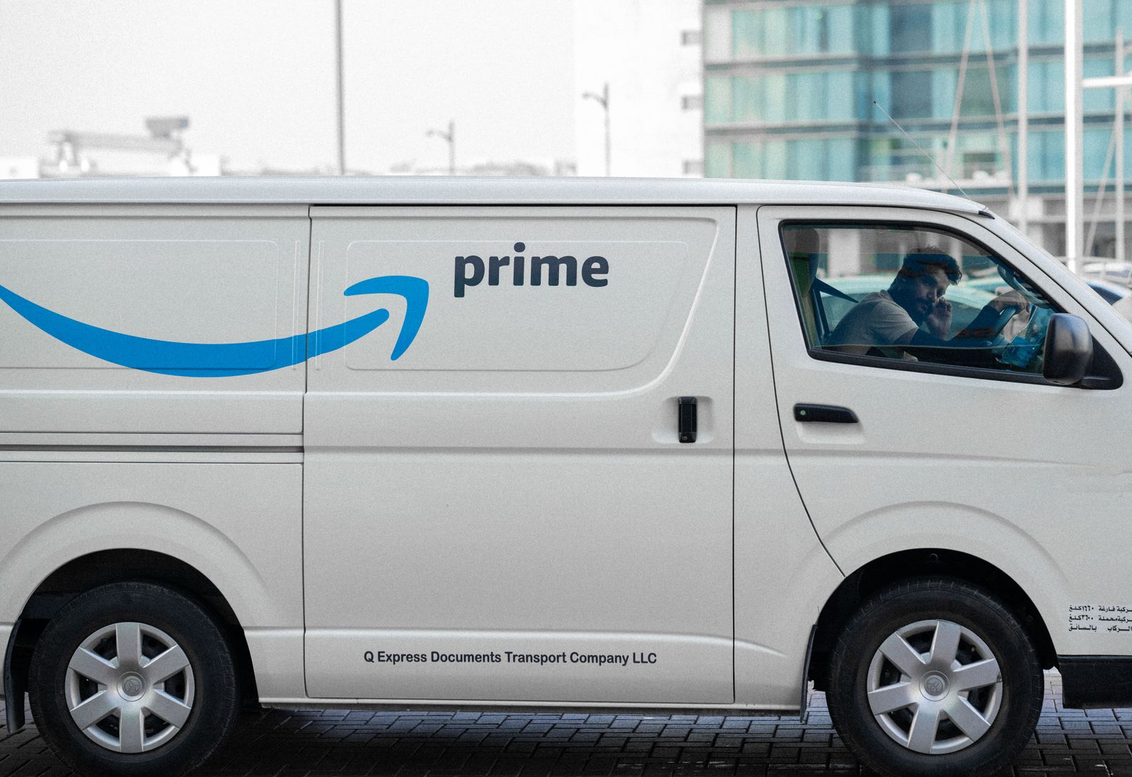 A white delivery van with Prime logo parked on an urban street with driver inside.