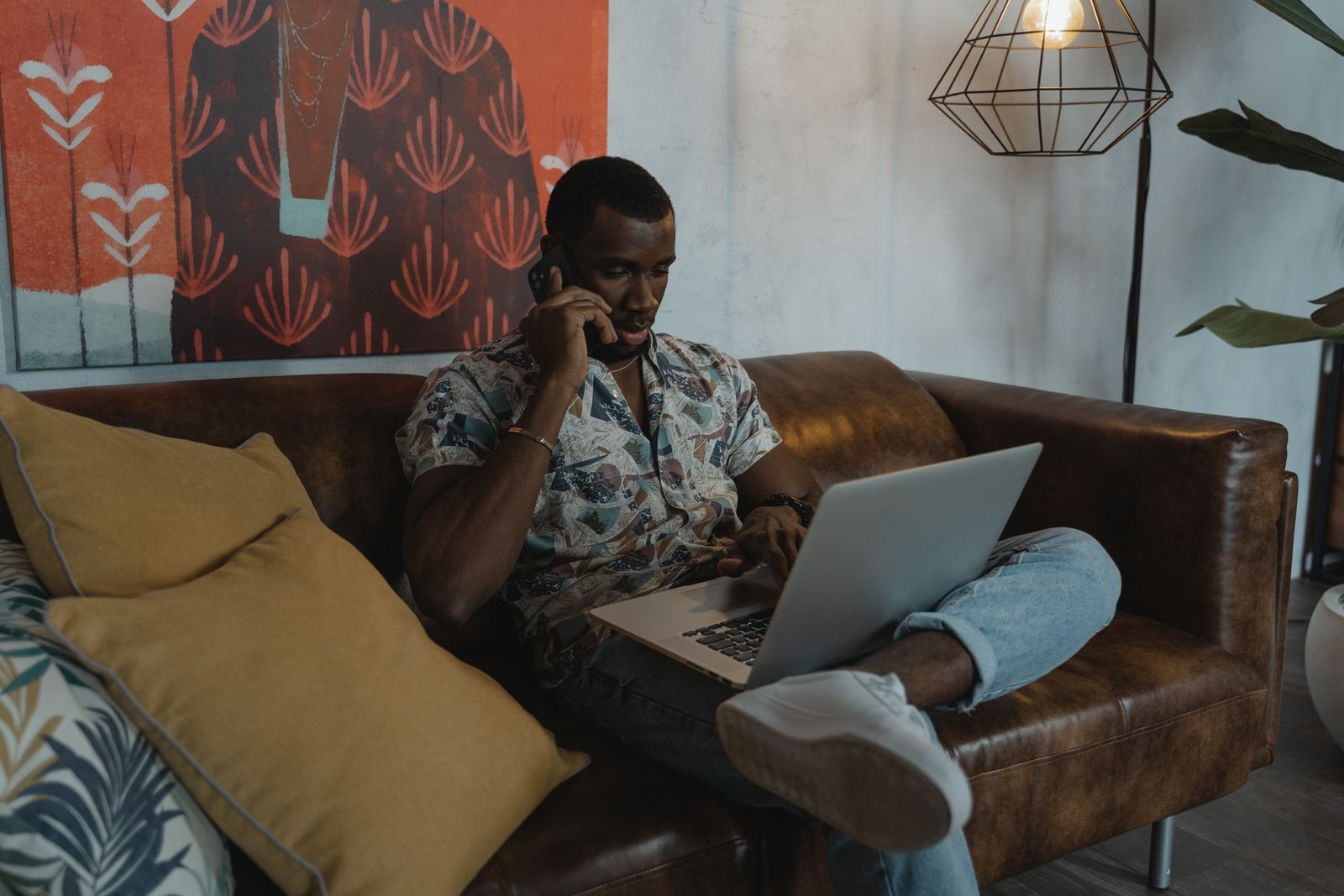 Man working remotely from home on a laptop while talking on the phone. Stylish and relaxed environment.