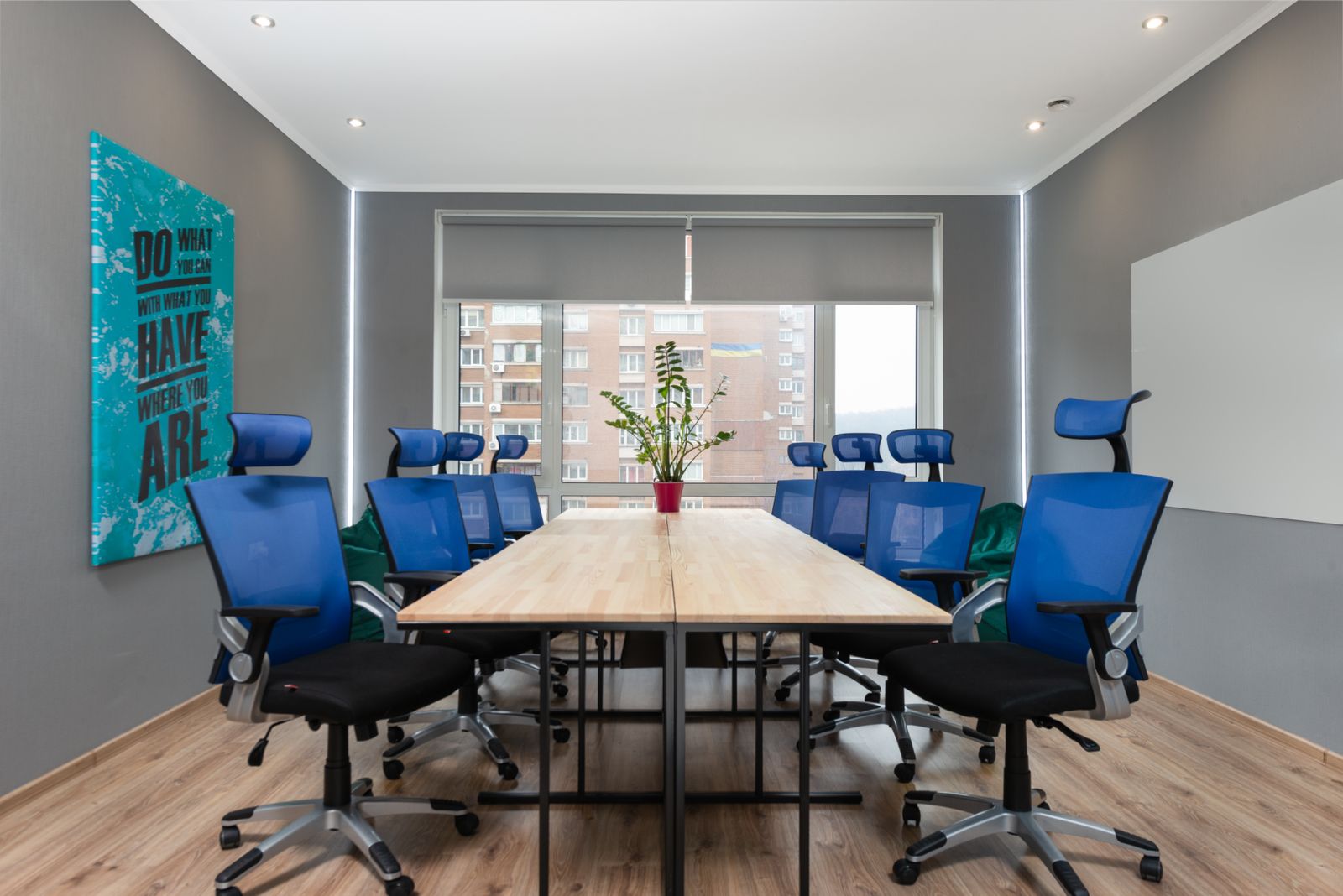 Armchairs at table with green plant placed near wall with creative signboard in modern conference room with window in office
